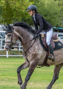 Equestrian rider jumping a horse while wearing Espoir show jacket, showcasing athletic fit, flexible fabric, and elegant competition styling